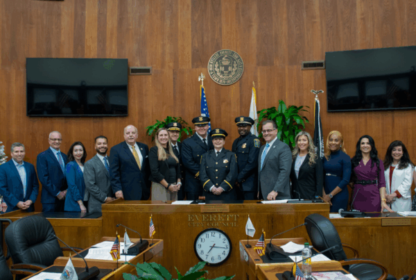 Promoted police officers pose for a group photo with the mayor, police chief, a state senator, and City Councilors at the City Council dais in the Council Chamber.