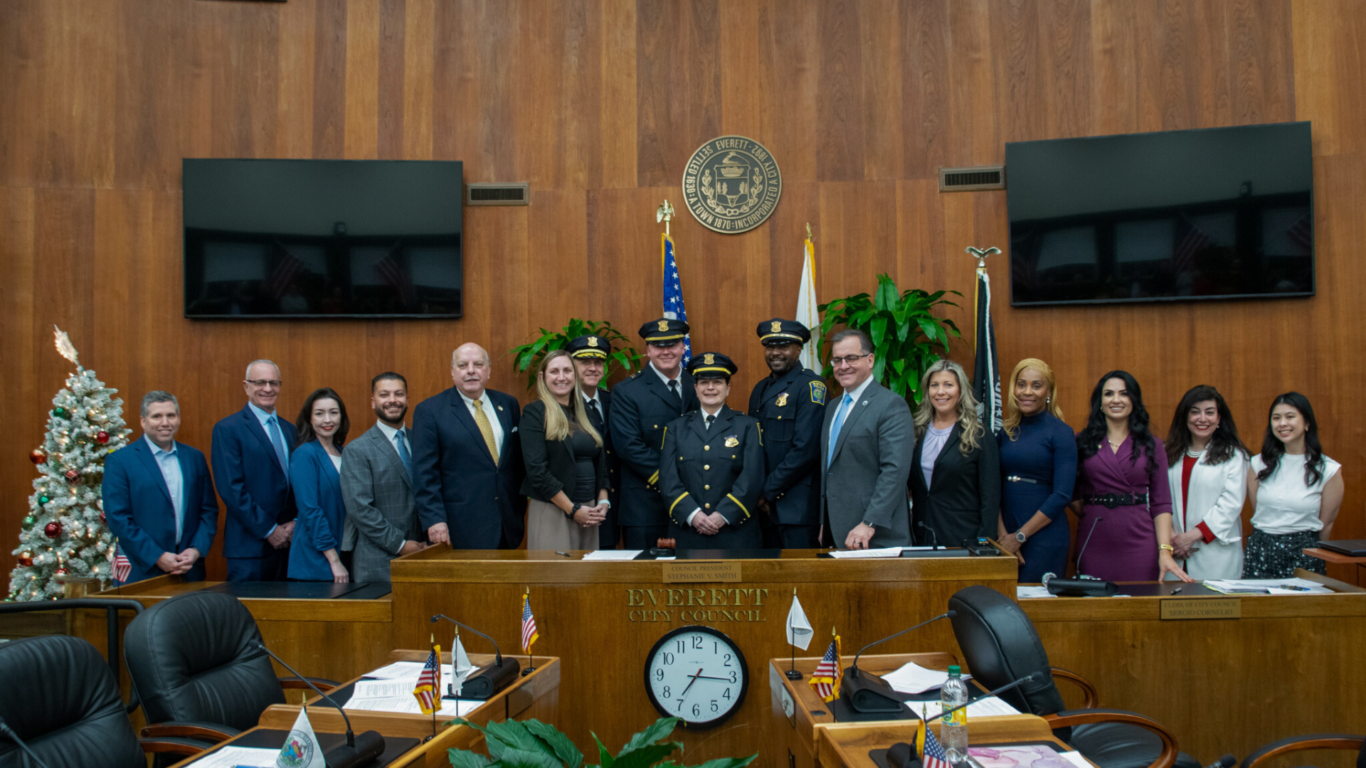 Promoted police officers pose for a group photo with the mayor, police chief, a state senator, and City Councilors at the City Council dais in the Council Chamber.