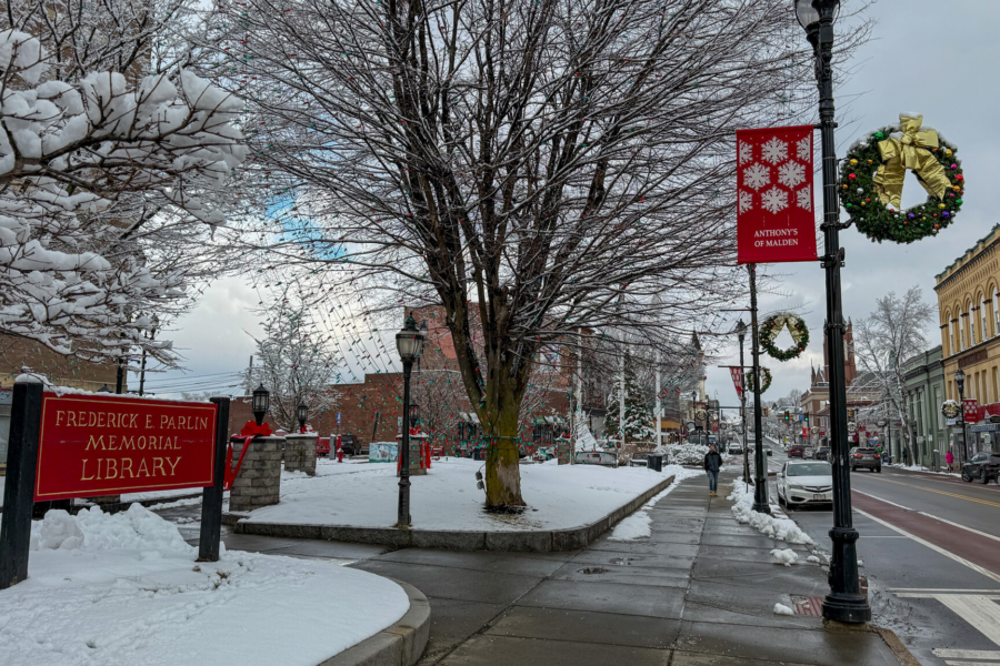 Snow-covered courtyard outside the Parlin Memorial Library, with trees, holiday wreaths on street lamps and a wet sidewalk along Broadway in Everett.