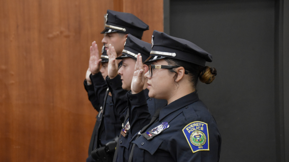 Everett police officers standing in a row with their hands raised as they take the pledge.