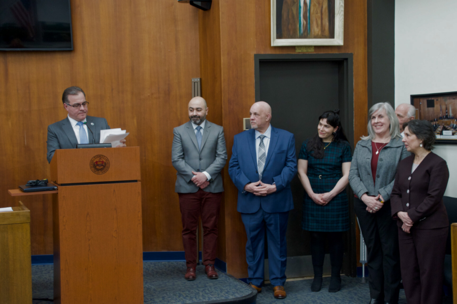 Mayor Robert Van Campen stands at a podium inside the Everett City Council Chamber as he reads from a piece of paper. Standing alongside him is his senior staff that he is introducing to the audience.
