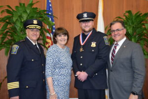 Chief Strong, District Attorney Marian Ryan, Mayor Robert Van Campen all pose for a photo with Detective Wall in chambers 