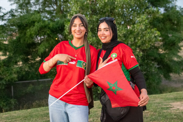 Two Morocco fans pose with team gear and a Moroccan flag.