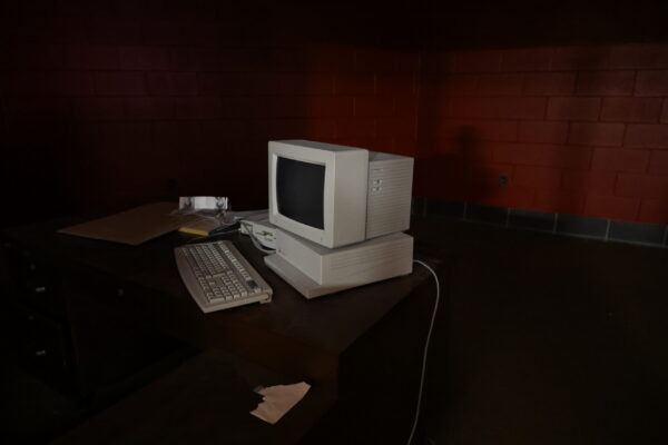A computer monitor from the early 2000s sits on a desk in am empty room