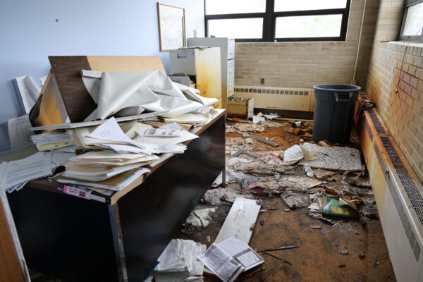 A small room with a desk covered in papers and trash