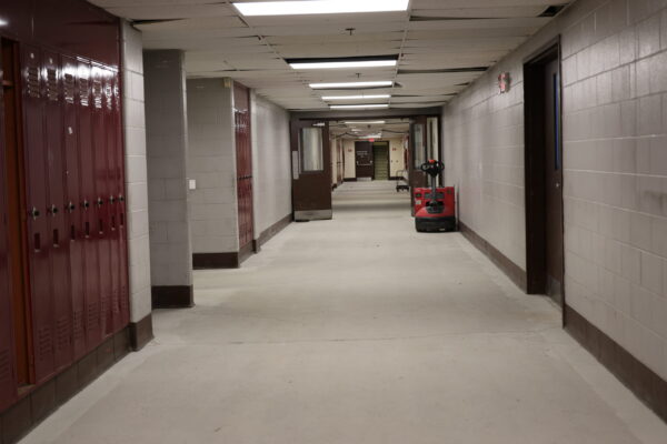 Empty Hallway lined with red lockers showing the tiles removed down to the cement.