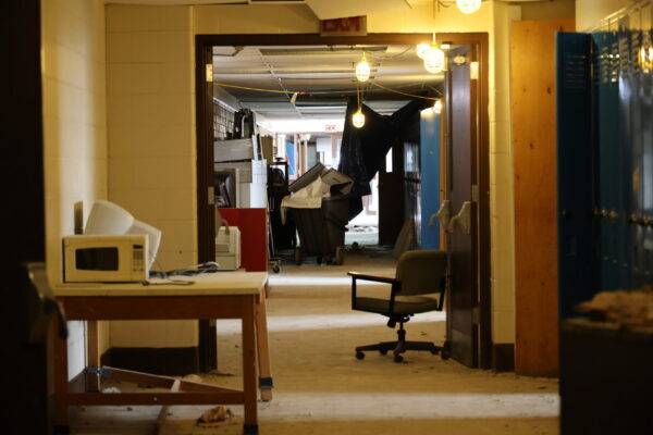 Peering down a hallway you can see the roof collapsed surrounded by old furniture and trash